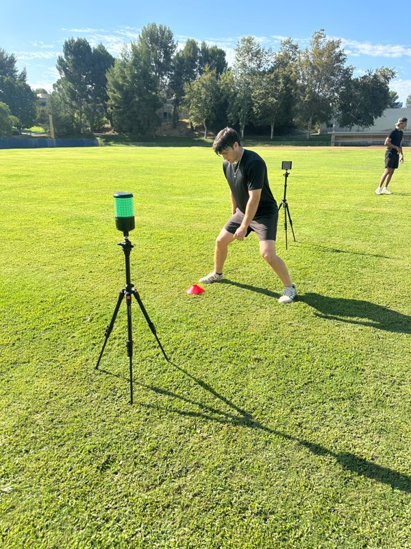 An athlete starting a sprint next to a timing gate on a grass field.